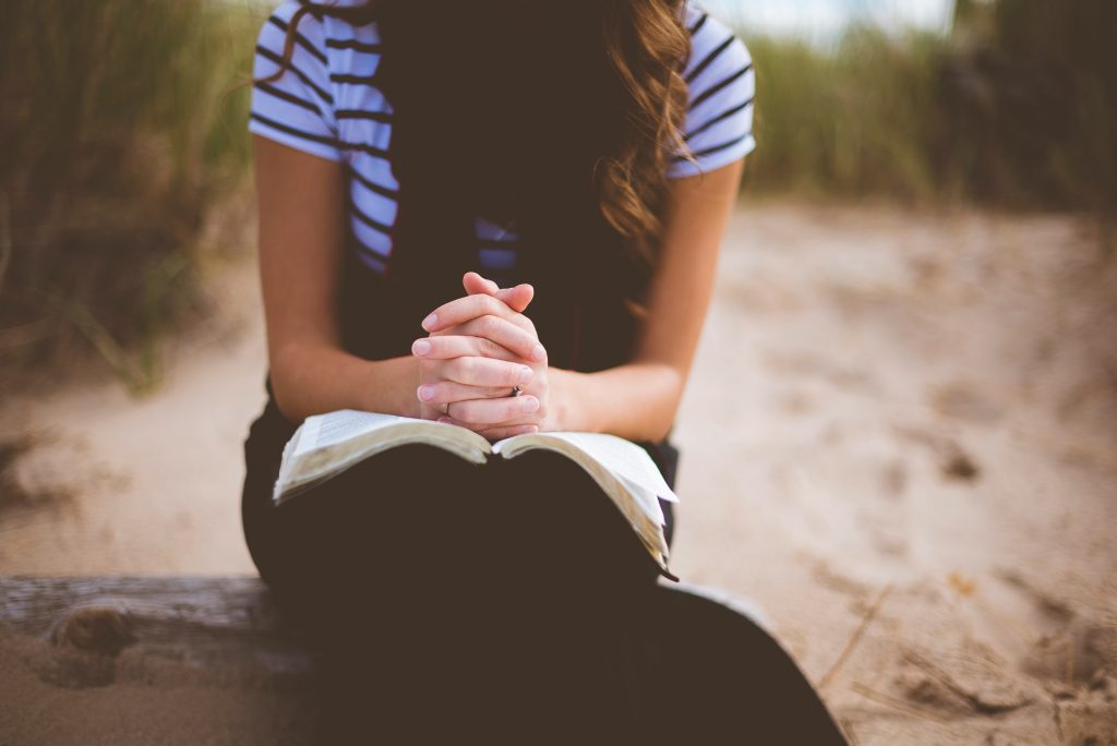 Femme en prière les mains jointes sur une Bible ouverte — marcher avec Dieu dans une relation intime