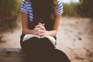 Femme en prière les mains jointes sur une Bible ouverte — marcher avec Dieu dans une relation intime